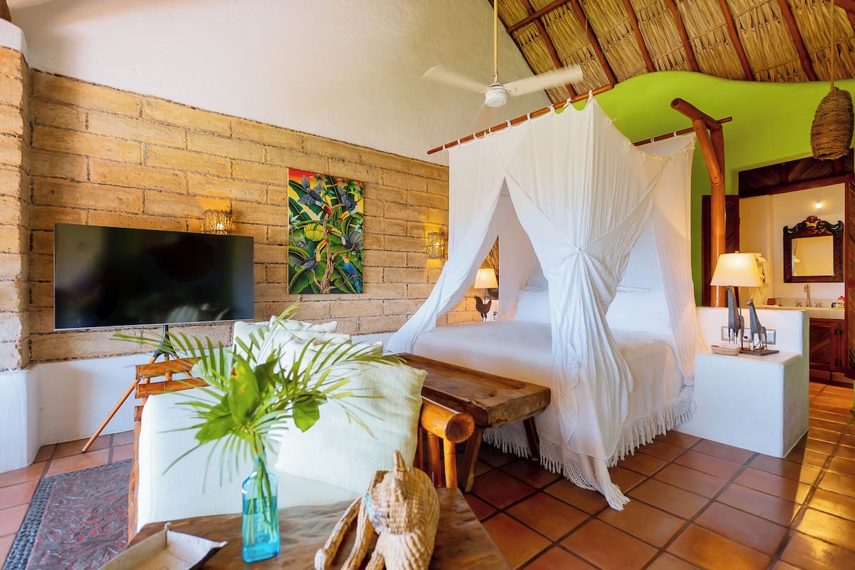 A room with a brick wall, a flat-screen TV, a bed with a canopy, a wooden table, and a potted plant.