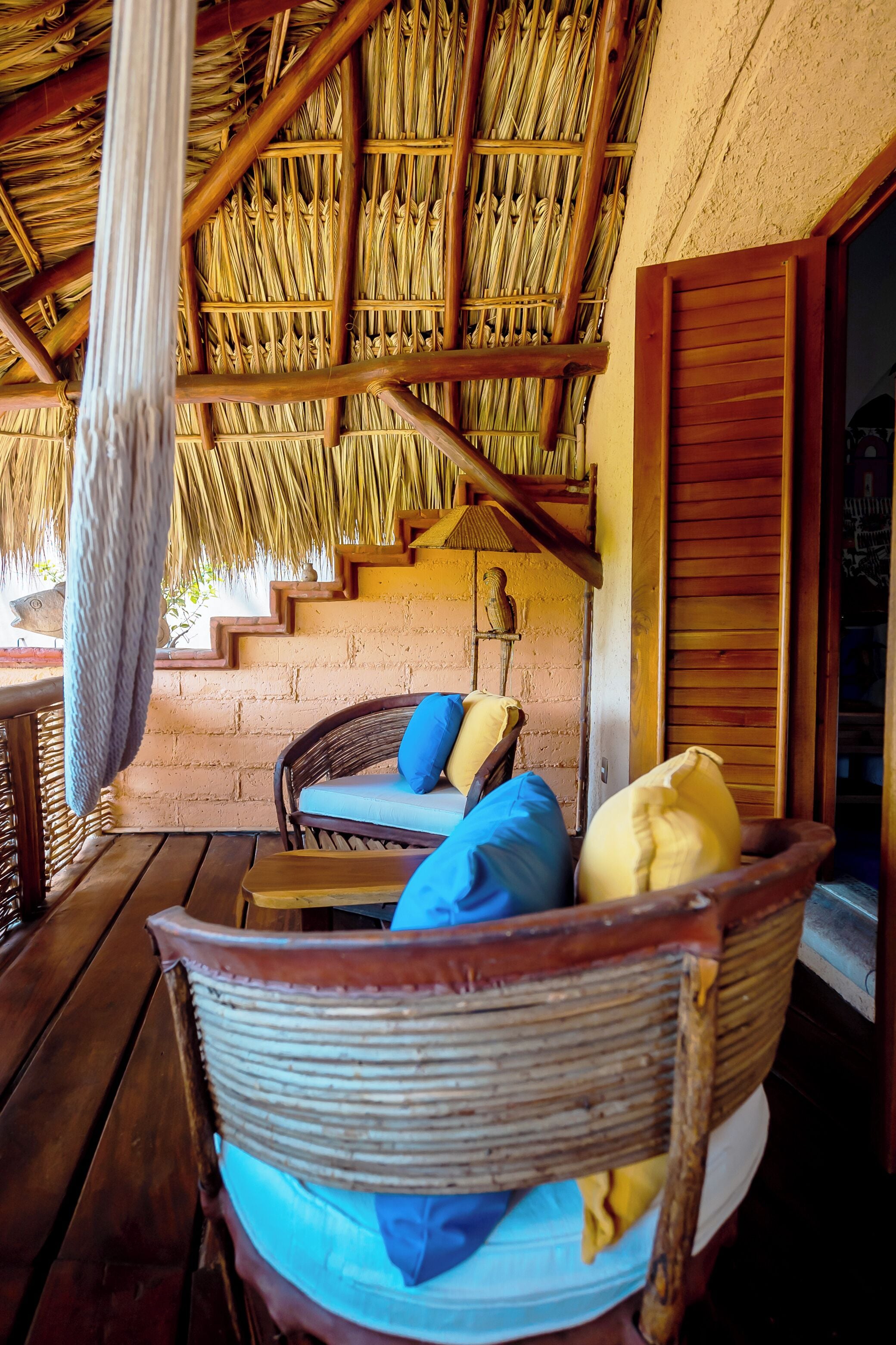 A wicker chair with cushions, a thatched roof, and a wooden staircase.