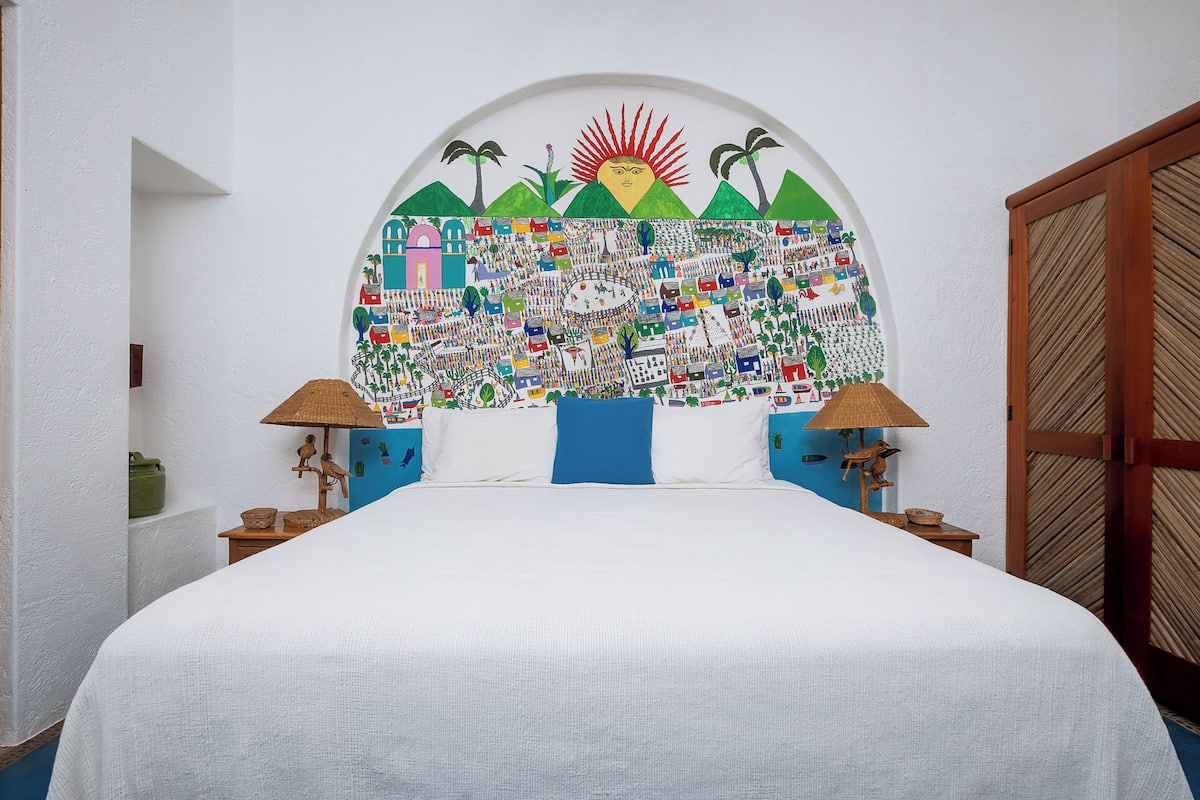 A bedroom with a large bed, two nightstands, a wall mural, and a wooden wardrobe.