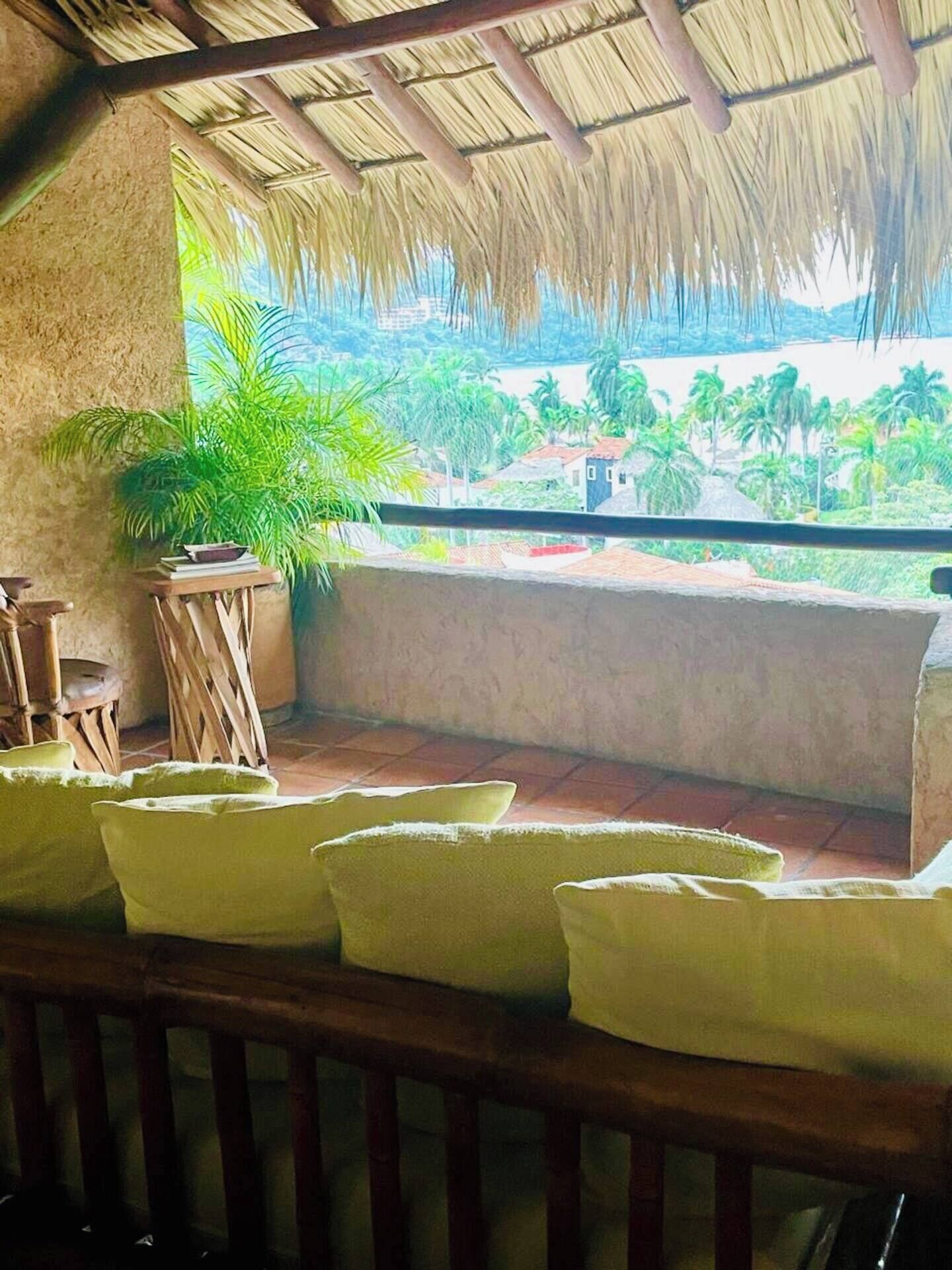 A balcony with a thatched roof, a potted plant, and a seating area with cushions.