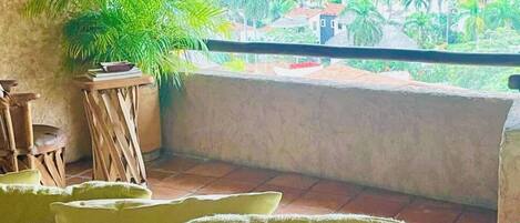A balcony with a thatched roof, a potted plant, and a seating area with cushions.