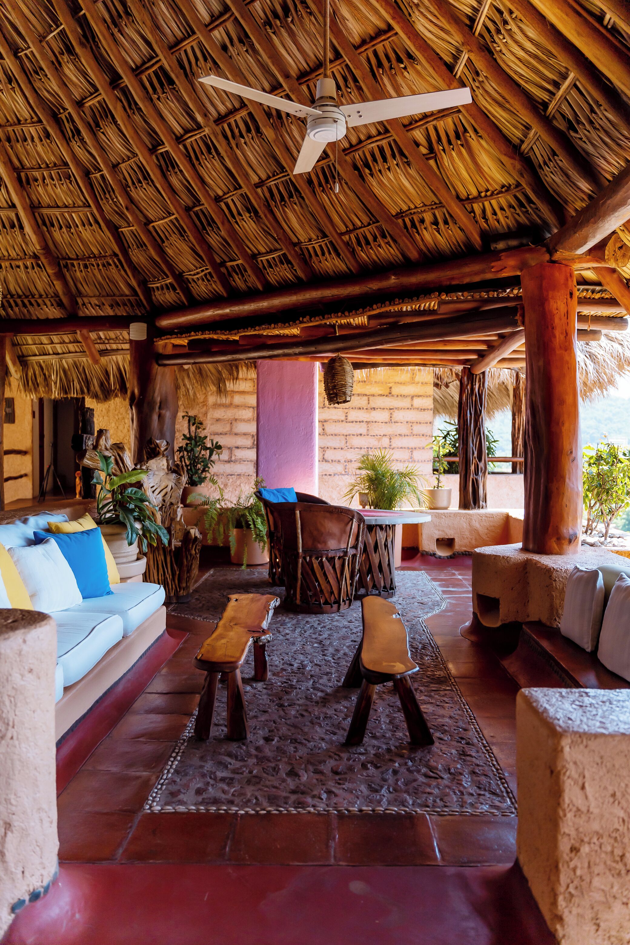 An open-air lounge with a thatched roof, wooden furniture, and potted plants.