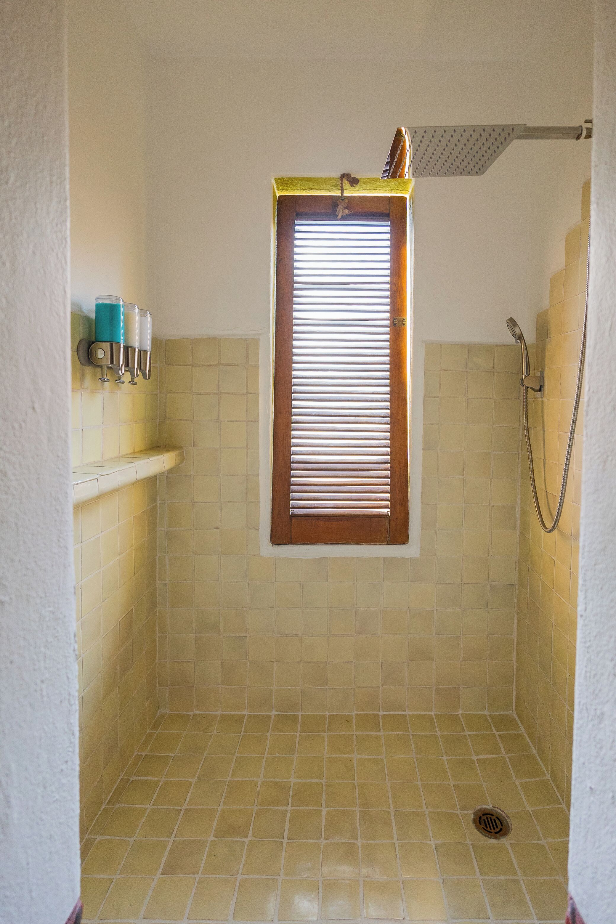 Un espacio de ducha pequeño y cerrado, con ventana, paredes de azulejos y ducha.