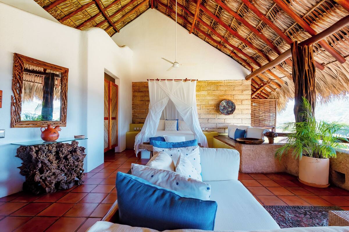 A room with a bed, a wooden table, a potted plant, and a brick wall.