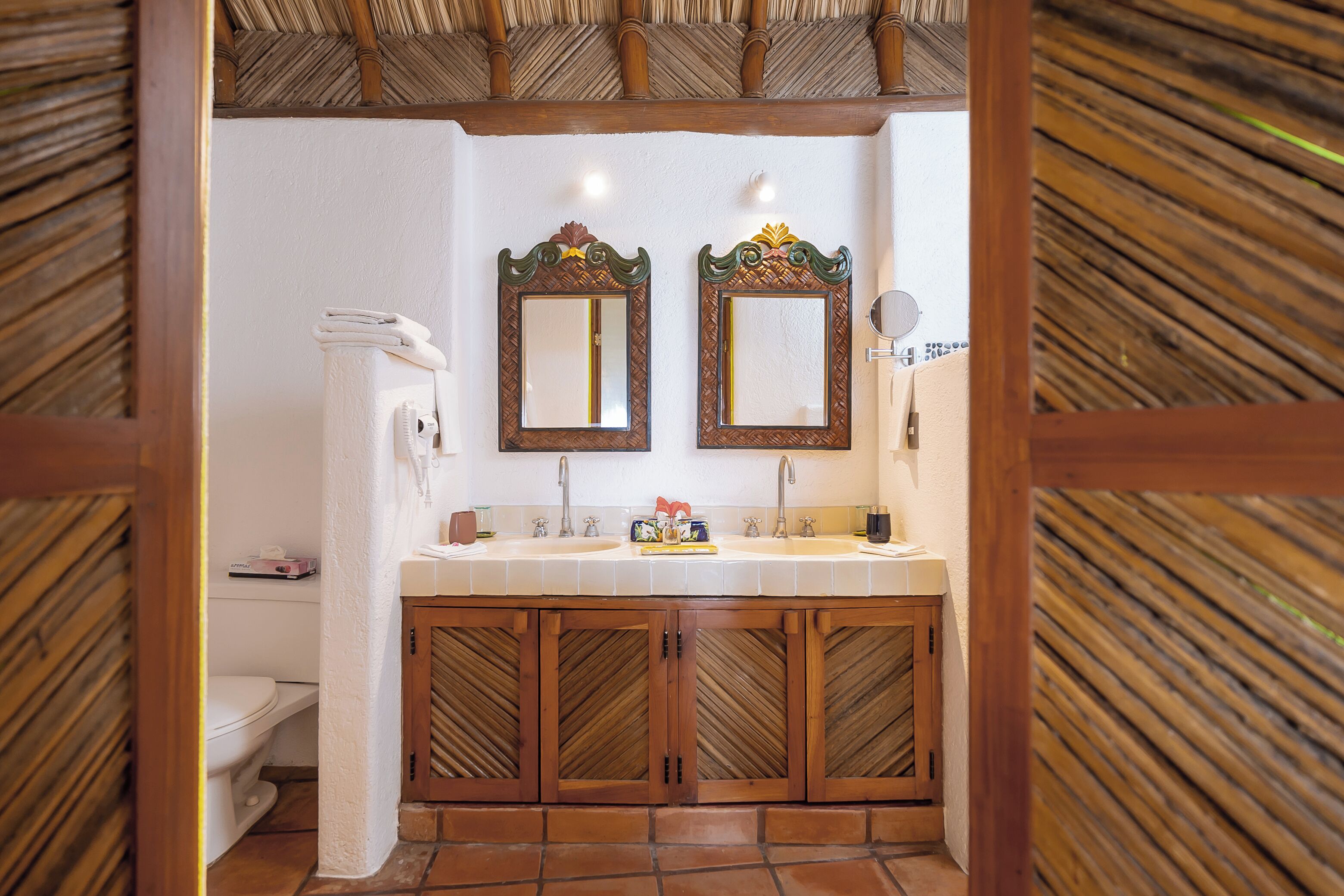 A bathroom with a wooden vanity, two mirrors, a toilet, and a towel rack.