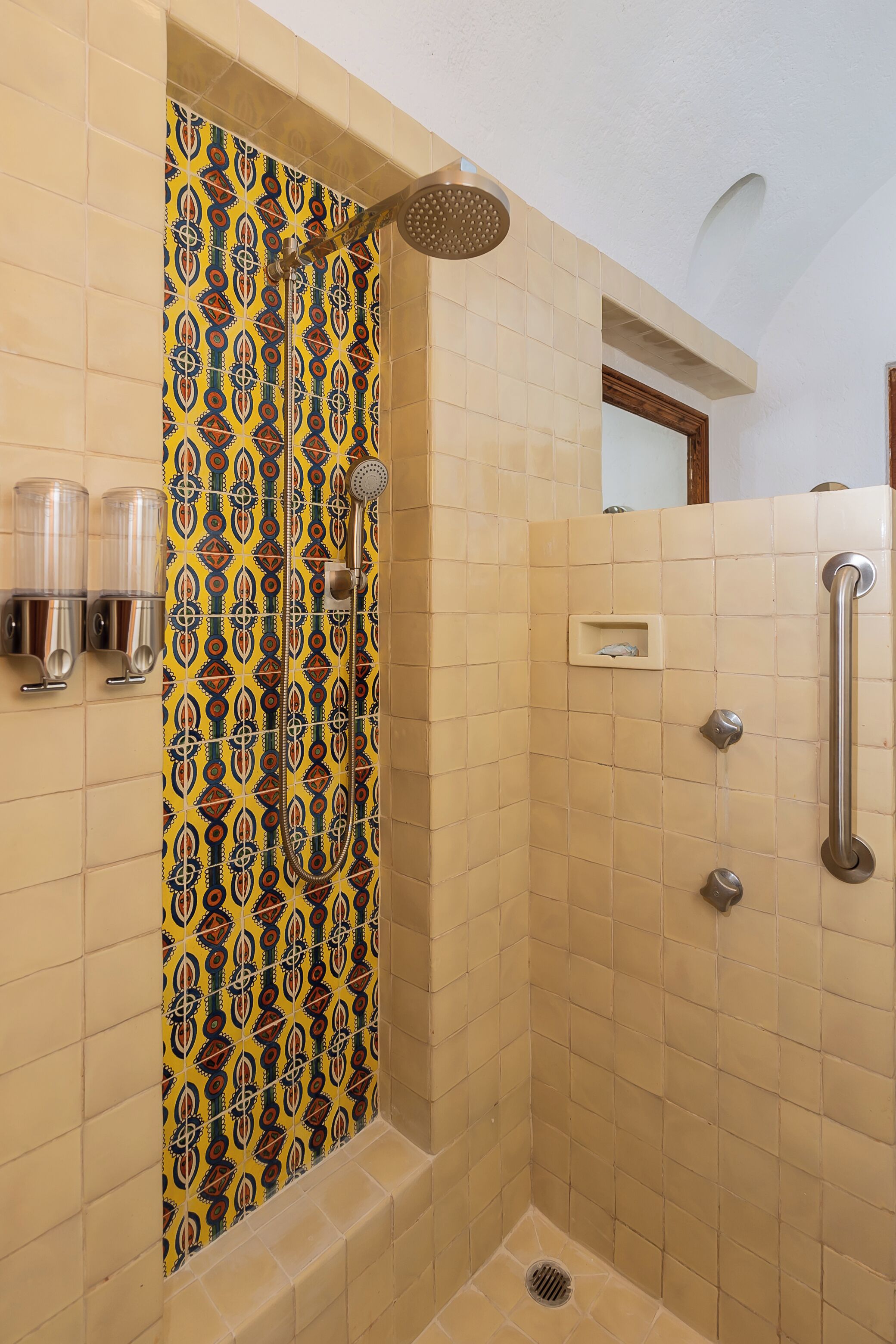 A shower with a patterned tile wall, a handrail, and a showerhead.