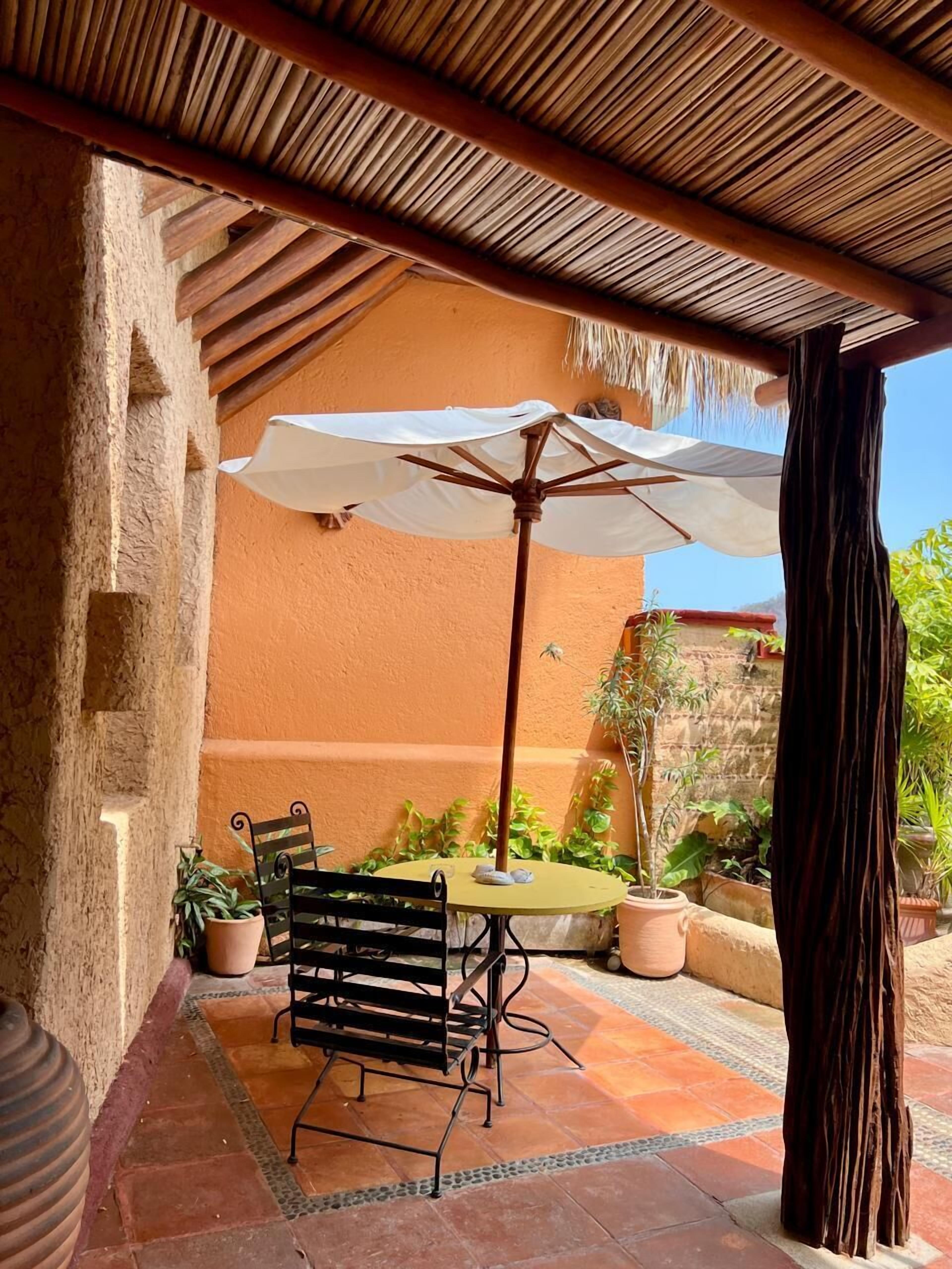 Une terrasse extérieure avec une table et deux chaises, un grand parasol et des plantes en pot.