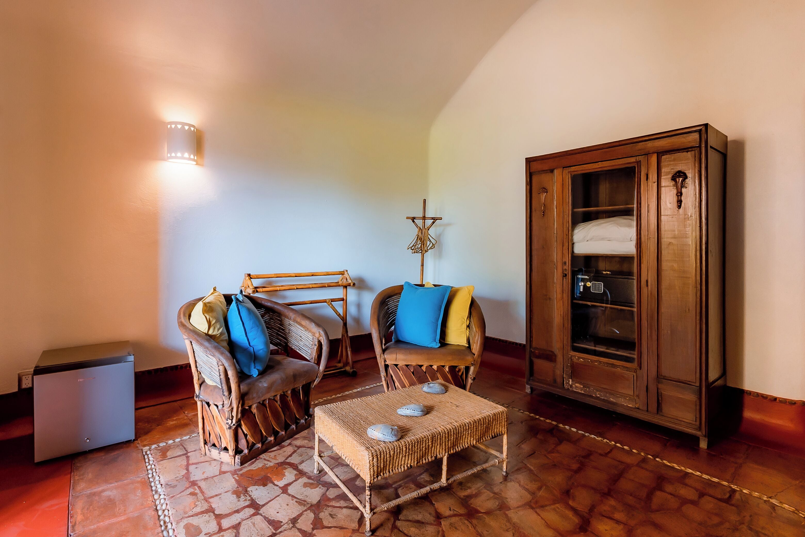 A room with a wooden cabinet, wicker chairs, a small table, and a wall-mounted light fixture.