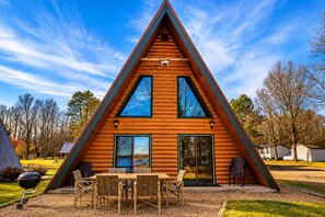 A triangular wooden cabin with a patio area featuring a grill and outdoor furniture.