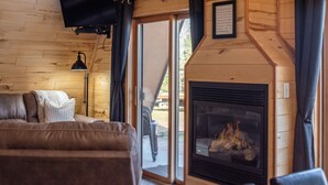 Een knus ingerichte kamer met een open haard, een bank en een aan de muur bevestigde televisie.