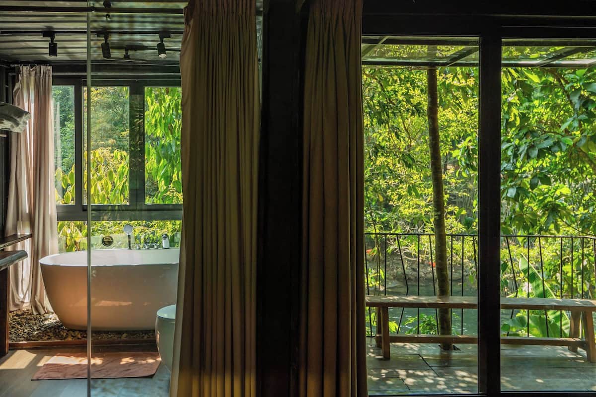 A bathroom with a bathtub, a sink, and a window overlooking a lush garden.