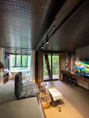 A room with a bed, a television, a desk, and a window overlooking greenery. - YesHue Eco Waterfall Retreat (Hue)