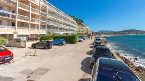 A multi-story hotel with balconies, parked cars along the beachfront, and a clear view of the sea.