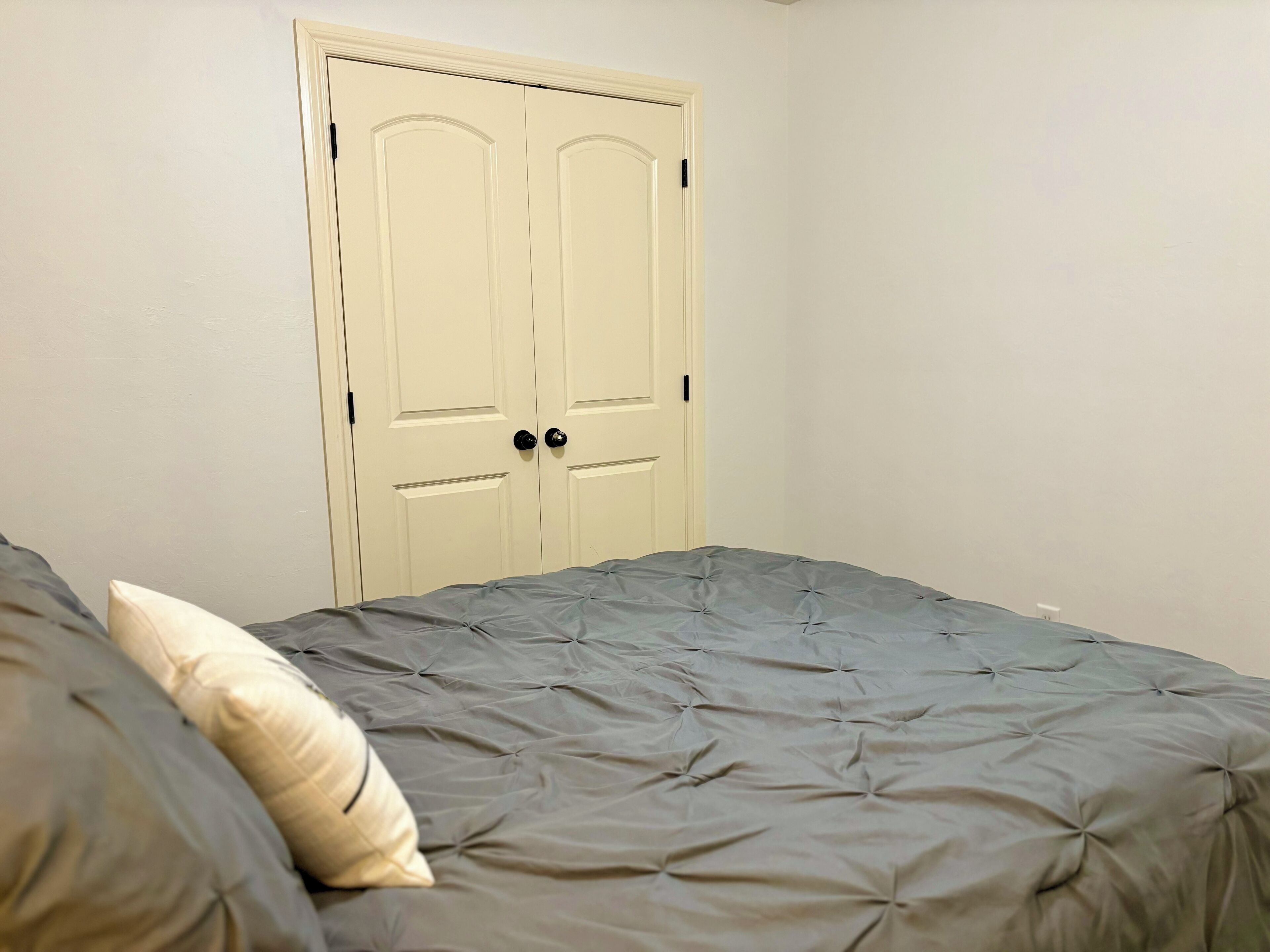 A bedroom with a bed, two doors, and a white wall.