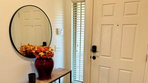 A white door with a black handle, a round mirror, and a vase with autumn leaves on a wooden console table. - Beautiful Cozy Edmond Home - 4bed 2bath (Edmond)