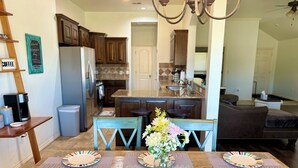 A dining area with a wooden table set for four, a vase with flowers, and a kitchen in the background. - Beautiful Cozy Edmond Home - 4bed 2bath (Edmond)