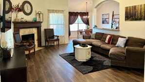 A living room with a fireplace, a ceiling fan, and a dining area with a table and chairs. - Beautiful Cozy Edmond Home - 4bed 2bath (Edmond)
