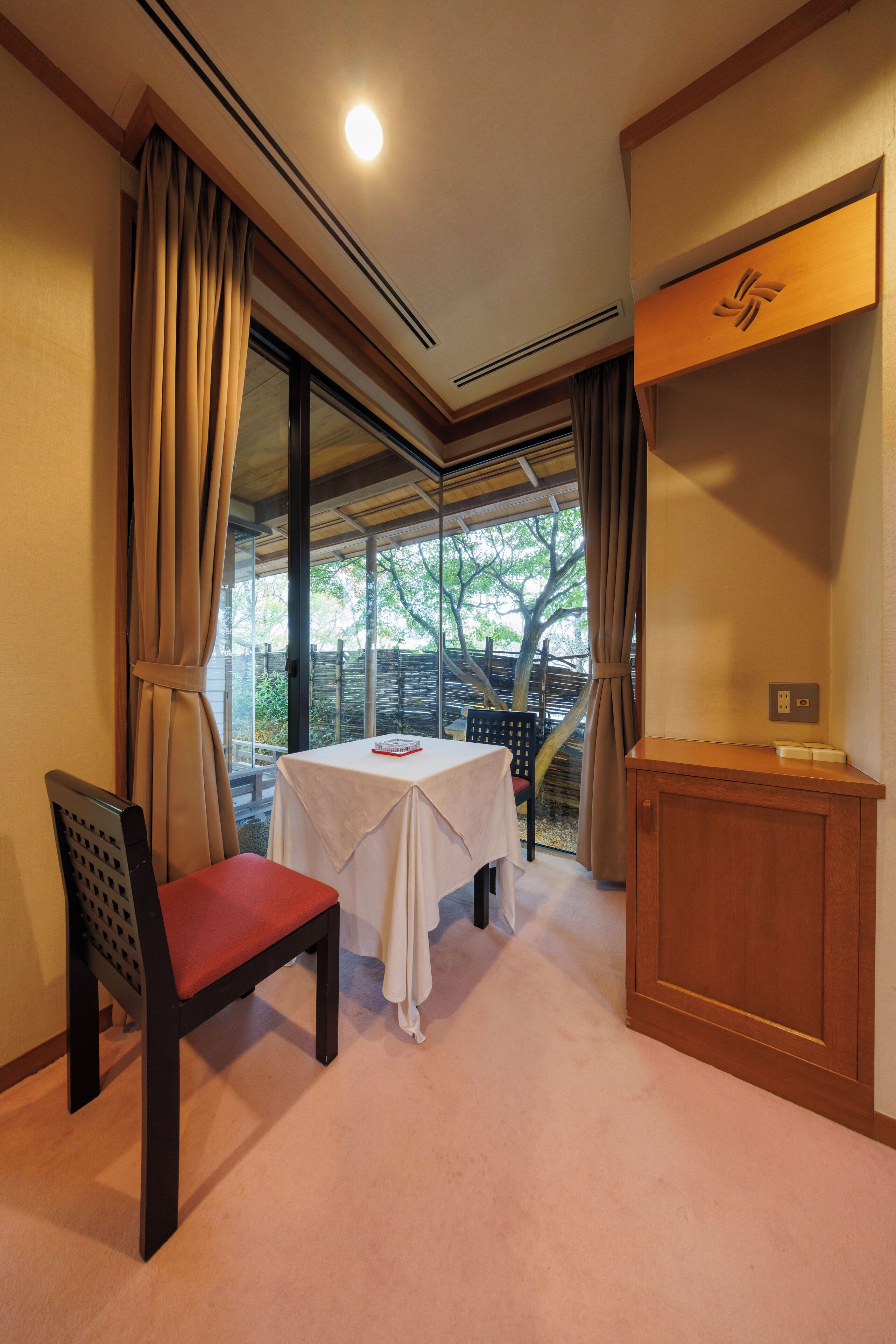 A room with a table, a chair, a cabinet, and a window with curtains.