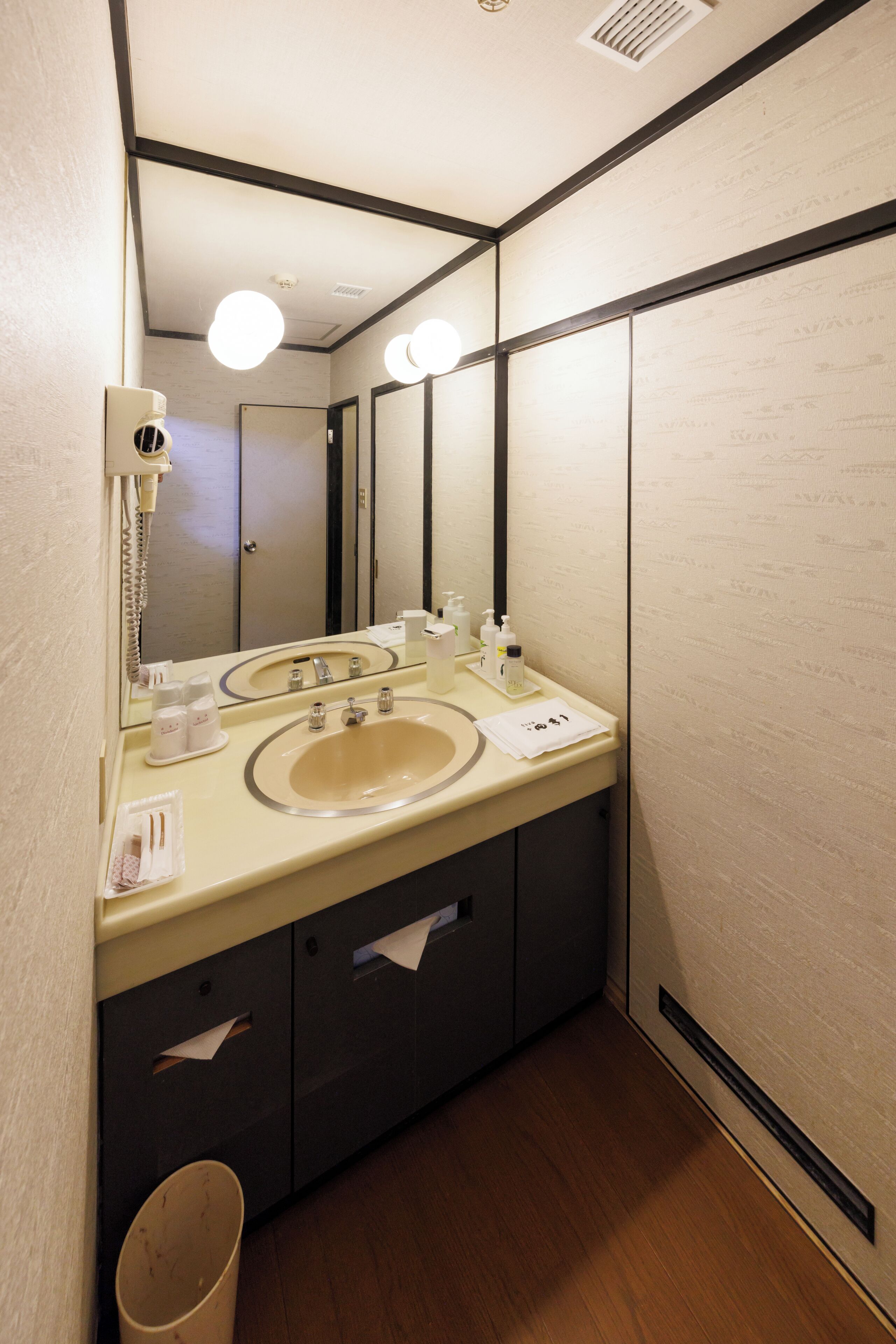 Une salle de bain d’hôtel équipée d’un double lavabo, d’un miroir, d’un sèche-cheveux et d’une poubelle.