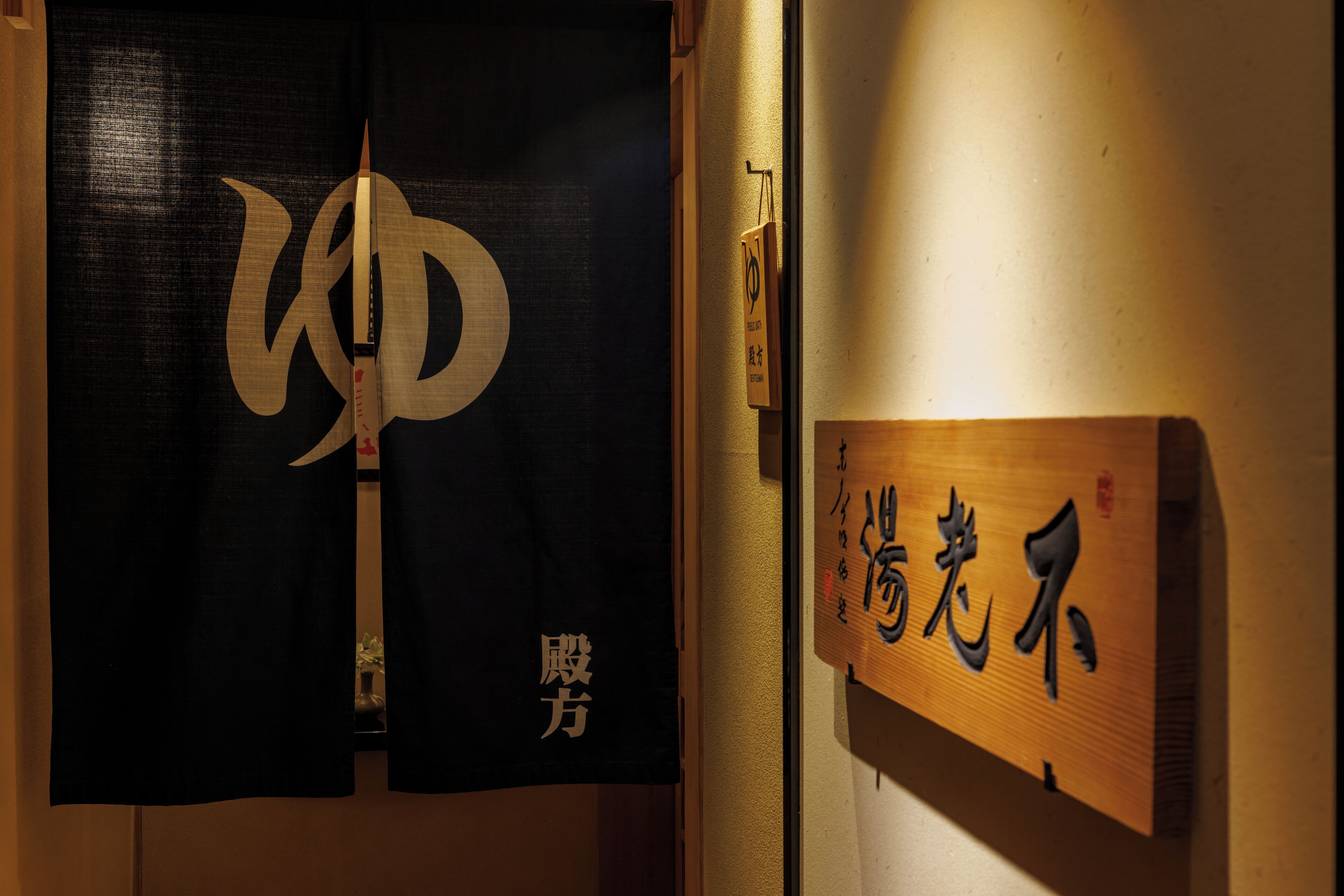 A wooden sign with Japanese characters, a black curtain with a large white symbol, and a small plaque on the wall.