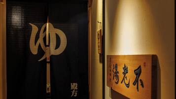 A wooden sign with Japanese characters, a black curtain with a large white symbol, and a small plaque on the wall.