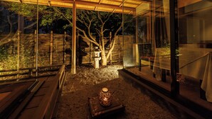 A modern outdoor space with a wooden bench, a decorative lantern, and a view of a tree through a glass wall. - Shikitei (Nara)