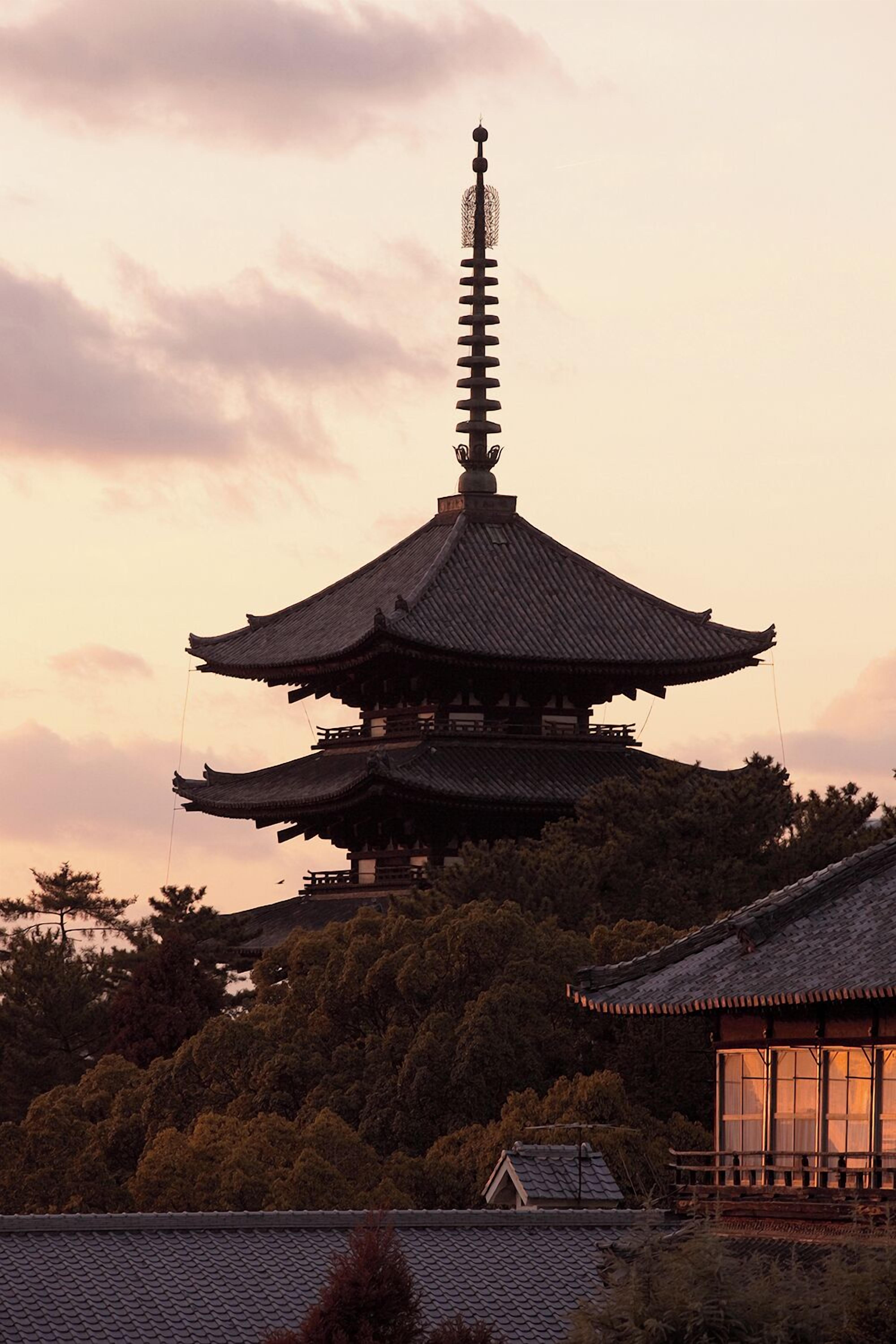 Un pagode japonés tradicional con varios niveles, rodeado de exuberante vegetación y un cielo despejado.