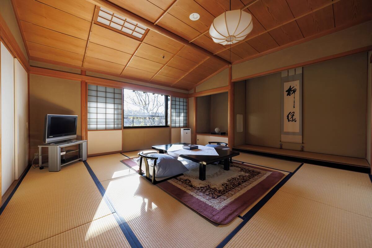 A traditional Japanese room with tatami flooring, a tatami mat table, a television on a stand, and a shoji screen.