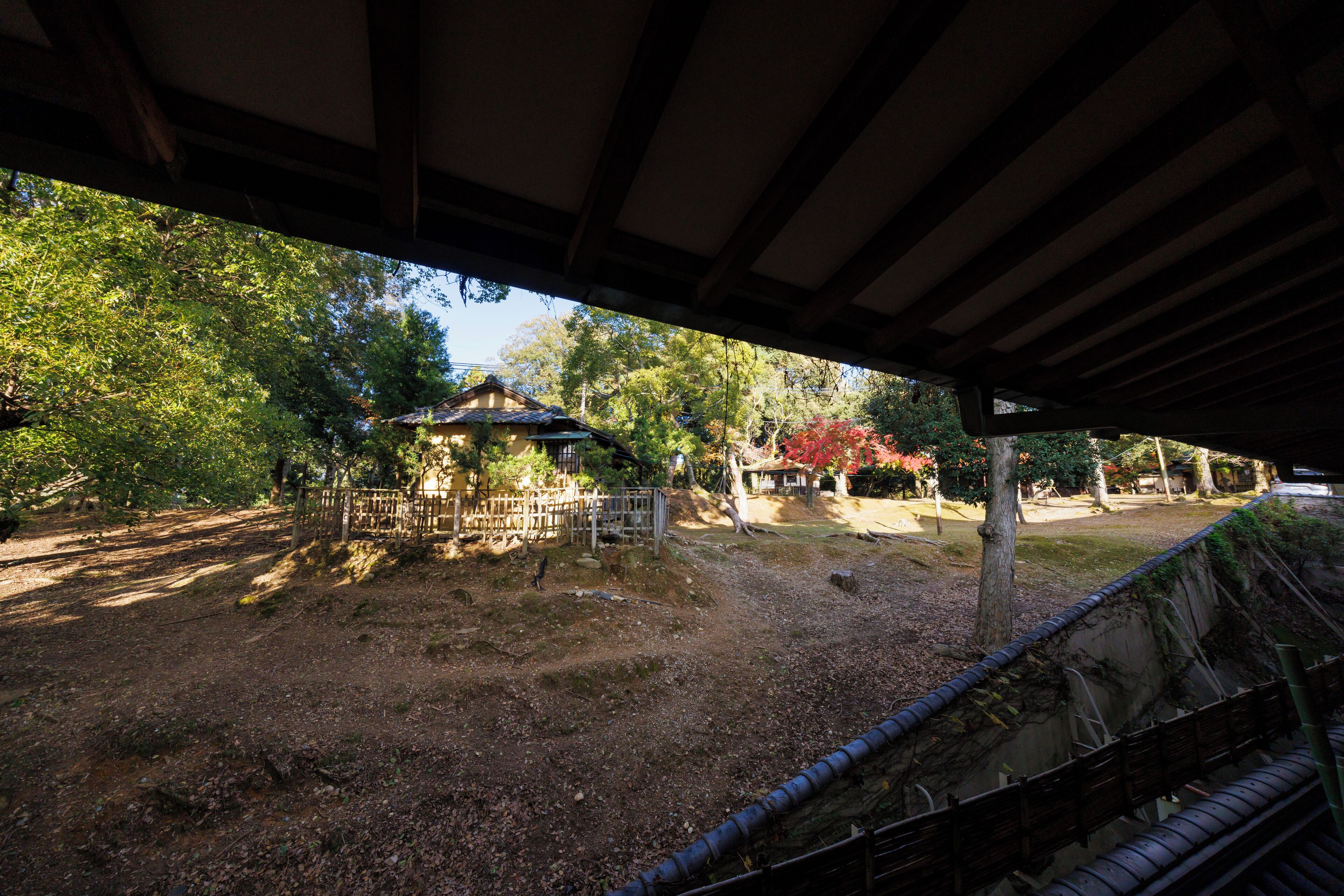 A covered outdoor area with a traditional Japanese structure, wooden benches, and a dirt path.