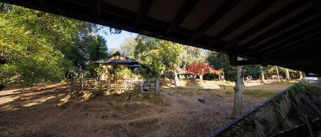 A covered outdoor area with a traditional Japanese structure, wooden benches, and a dirt path.