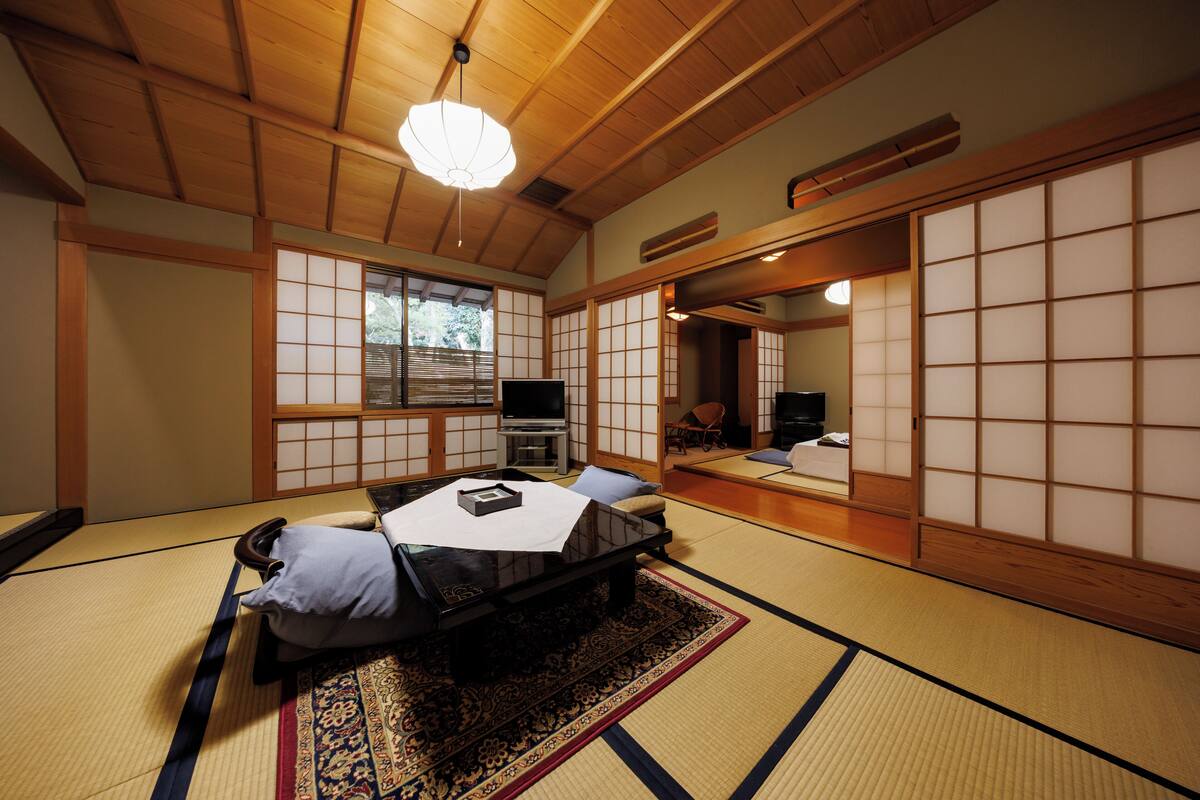 A traditional Japanese-style room with tatami flooring, a futon bed, a television, and sliding shoji doors.