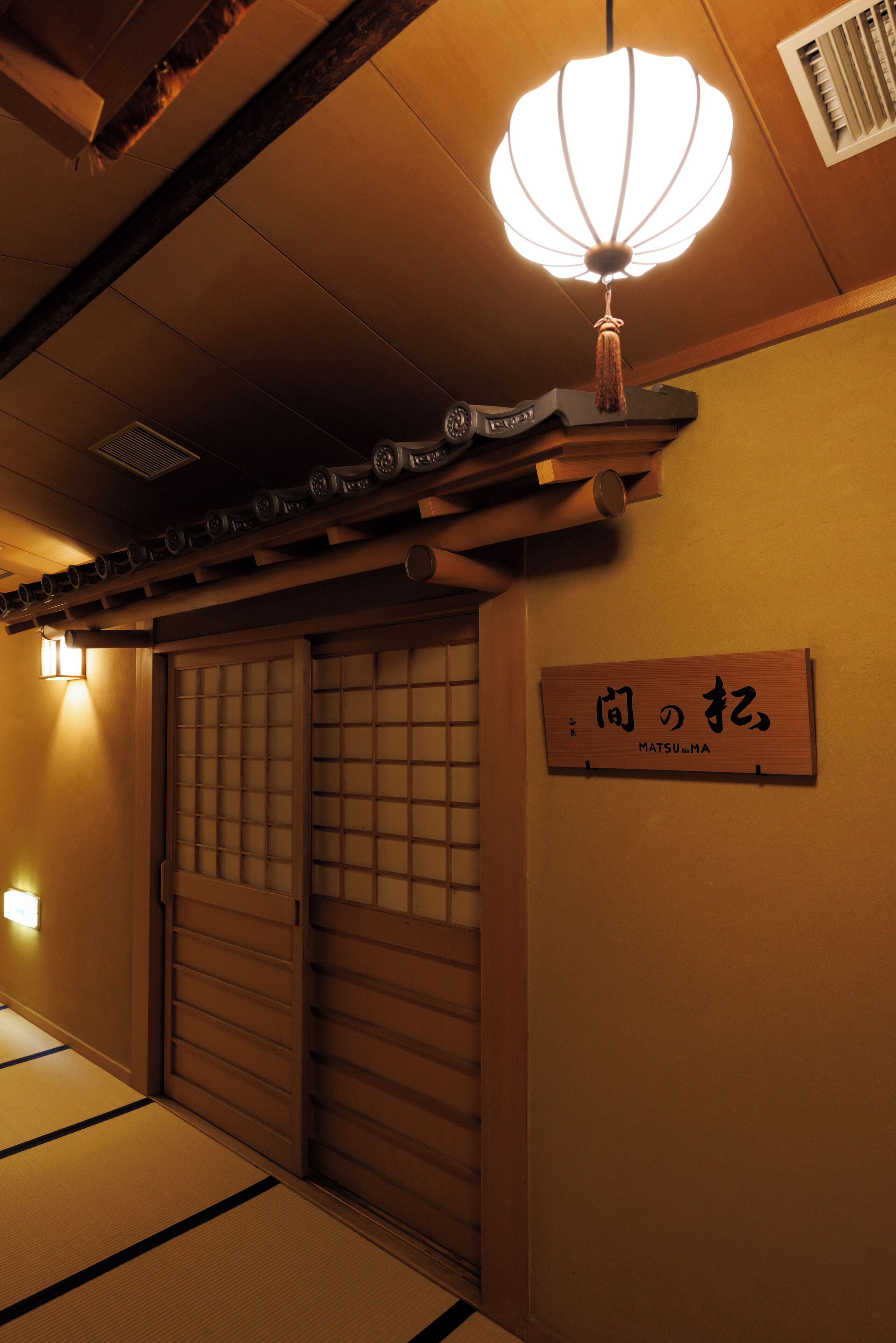 A traditional Japanese room with tatami flooring, a shoji screen door, and a hanging lantern.