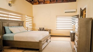 A bedroom with a bed, dresser, nightstand, and a small table with a chair. - North Ritz Villa (Ocho Rios, Draxhall, St. Ann)