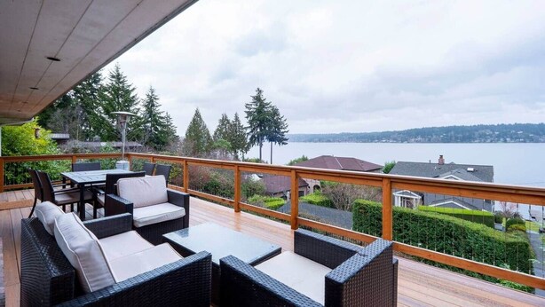 Eine überdachte Terrasse im Freien mit Korbmöbeln, Blick auf einen See und umgebende Grünflächen.
