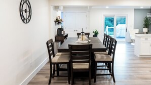 Uma sala de jantar com uma mesa retangular, seis cadeiras e um relógio fixado na parede.