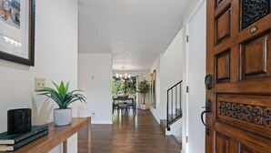Ein Korridor mit Holzboden, einem Blumentopf, einem gerahmten Bild und einem Essbereich im Hintergrund.