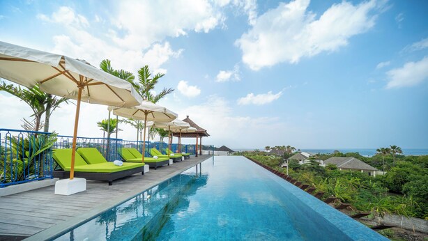 Un espace aménagé au bord de la piscine, avec des chaises longues et des parasols, donnant sur une étendue d’eau.