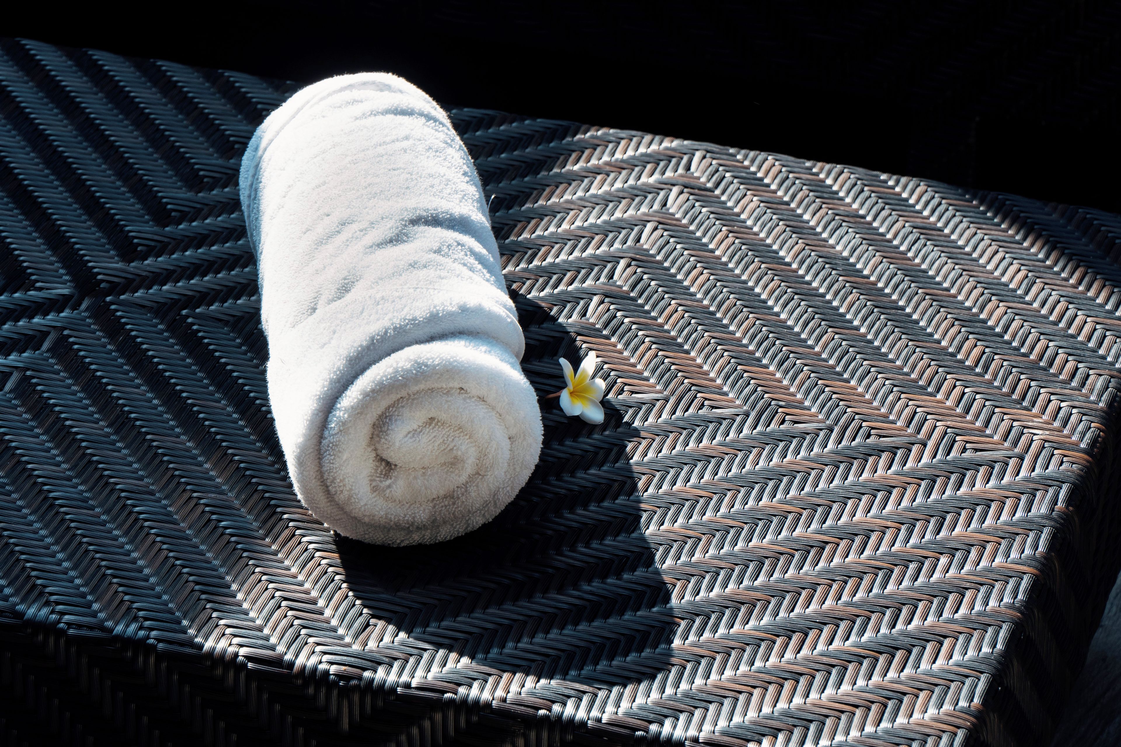 A rolled white towel on a woven surface with a small yellow flower.