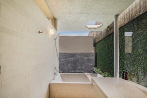 A modern bathroom with a large bathtub, a sink, and a wall covered in greenery. - Atap Beach Resort Canggu by Ini Vie Hospitality (Pererenan)