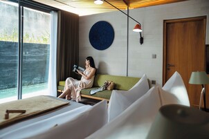 Una habitación con cama, sofá, lámpara de lectura y un amplio ventanal.