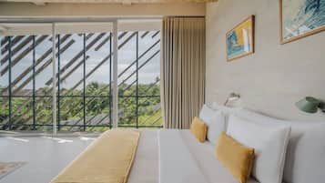 A hotel room with a large window, a bed with white bedding and a beige throw, and a green wall lamp.