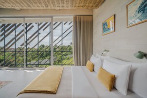 Una habitación de hotel con un ventanal grande, una cama con ropa de cama blanca y una manta color beige, y una lámpara de pared verde.