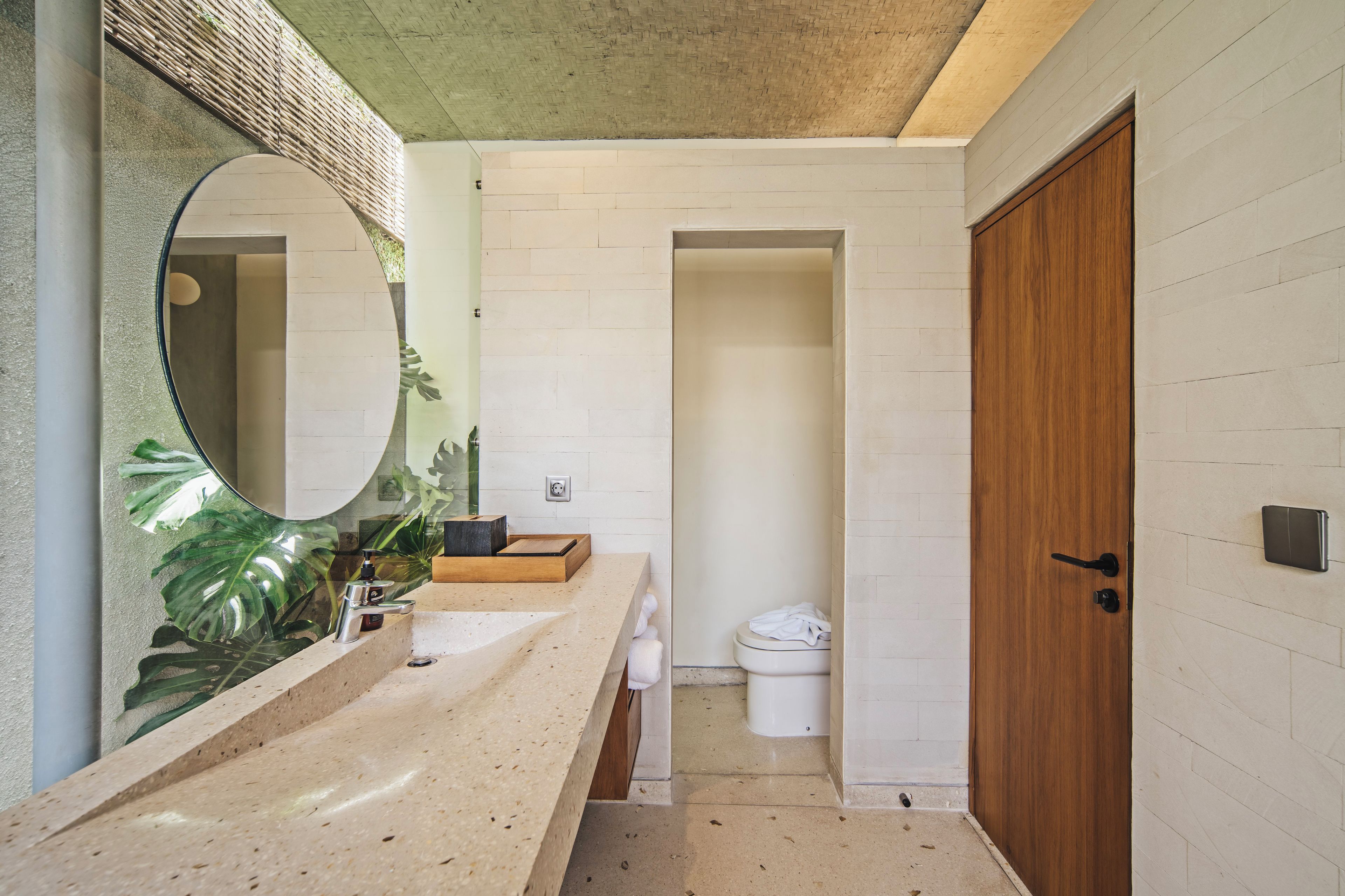 A bathroom with a large mirror, a sink, a toilet, and a wooden door.