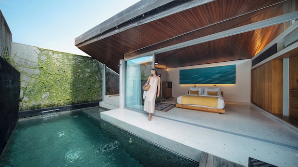 Un espace de vie extérieur moderne comprenant une piscine, une terrasse en bois et un espace clos par des parois de verre, avec un canapé et un téléviseur.