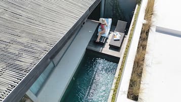 Zona de piscina en la azotea con una persona relajándose en una tumbona, rodeada de un diseño arquitectónico moderno.