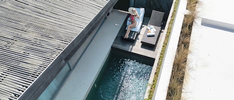 A rooftop pool area with a person relaxing on a lounge chair, surrounded by a modern architectural design.
