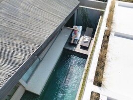 A rooftop pool area with a person relaxing on a lounge chair, surrounded by a modern architectural design.
