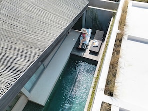 Zona de piscina en la azotea con una persona relajándose en una tumbona, rodeada de un diseño arquitectónico moderno.