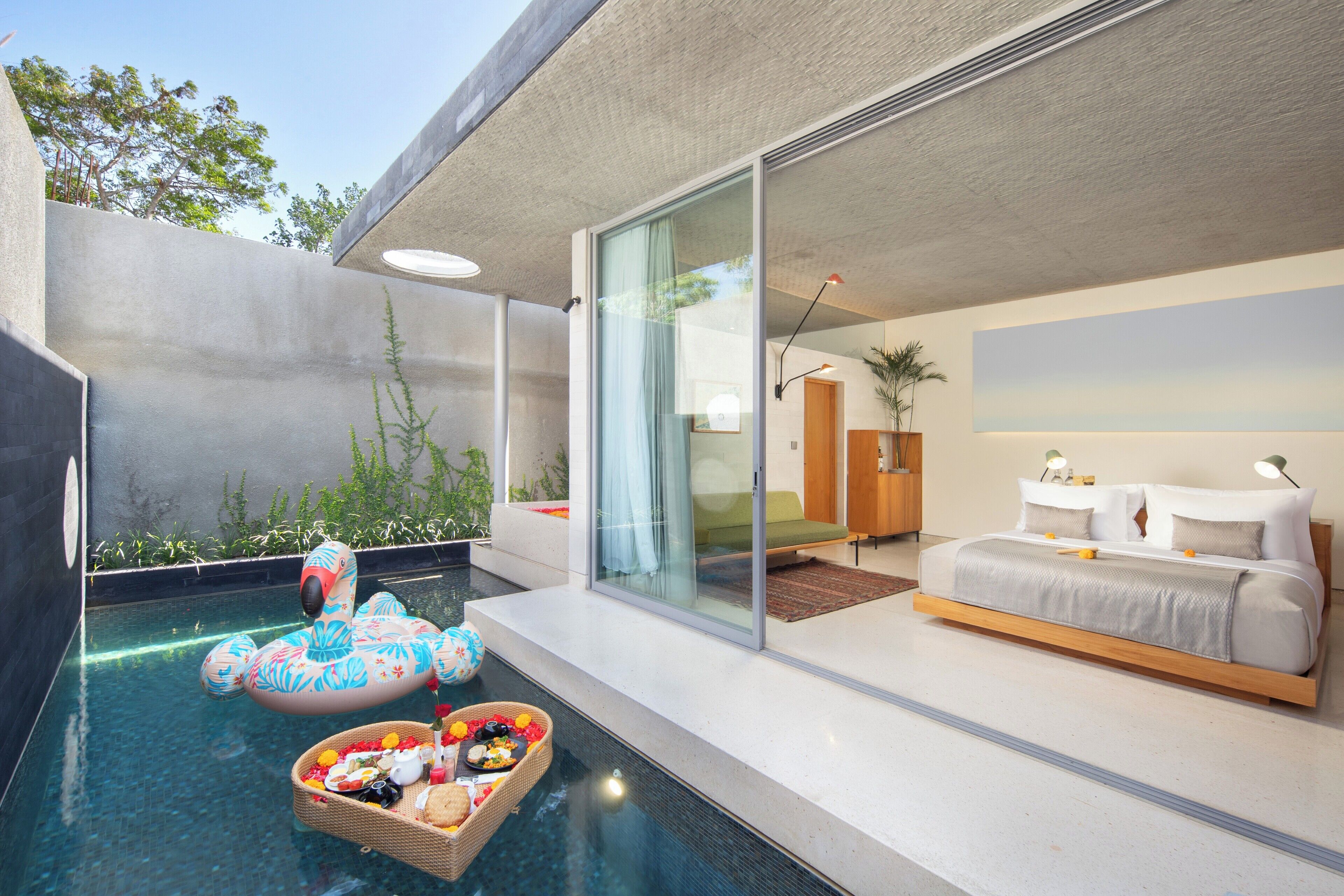 A modern bedroom with a large bed, a glass door leading to a balcony, and a swimming pool with a flamingo float.