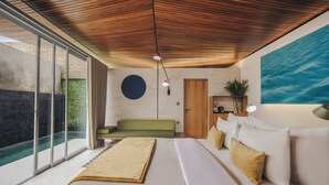 A modern hotel room with a large bed, a green sofa, a dining area, and a view of a swimming pool.